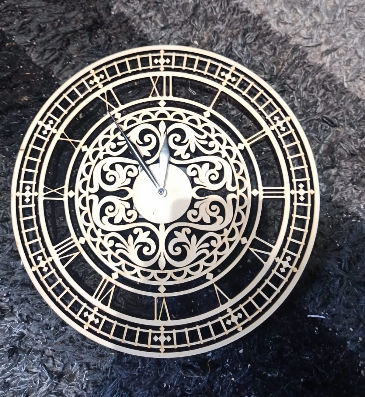 Laser-cut wooden wall clock with Roman numerals and ornate cut-out centre design